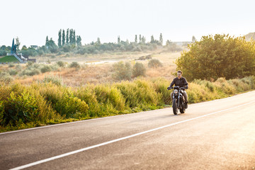 Obraz premium Young handsome man riding on motorbike at countryside road.
