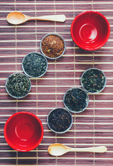 arrangement of tea leaves of different varieties of red cups and wooden spoons on bamboo Mat. Flat lay, top view