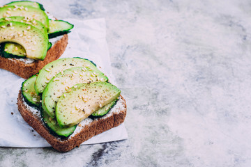 Healthy toast with cottage cheese, green cucumber and avocado on wooden board on a marble gray table background. Horizontal image, top view top, copy space. Vegetarian food content © Anikonaann