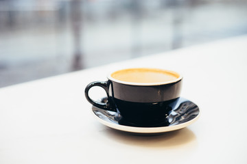 One cup with cappuccino on white marble countertop near big window.