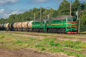 Fototapeta na wymiar Freight train with tank wagons moving in forest. Green diesel ca
