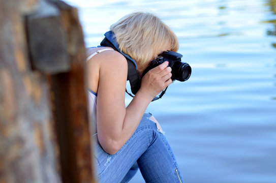 Woman photographer takes photo on her haunches on the background of water