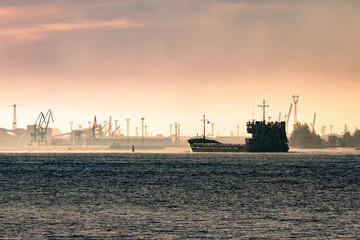 Fototapeta premium Cargo ship silhouette entering a port of Riga at the morning