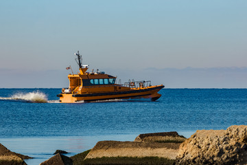 Yellow pilot ship moving at speed past the breakwater dam
