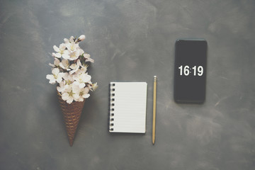 Flowers in ice cream cone with smartphone and notebook on cement background