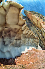 Scenic landscape of a rock and a wierd jagged snowfield on sunny summer day. Vertical fisheye scenery