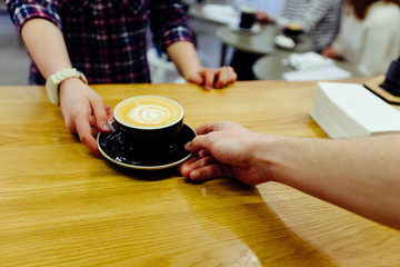 Fototapeta na wymiar Barista serving coffee to female customer in cafe. Close up of human hands touching with cup