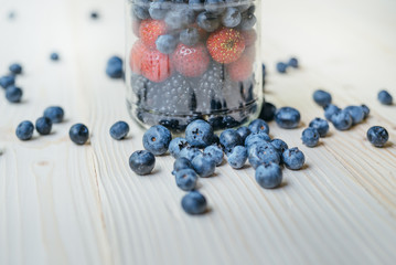 Rustic healthy breakfast with blueberry and strawberry in a glass jar on a wooden table. Glass of ripe berries. Healthy breakfast with vital vitamins.