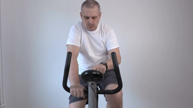 Man using exercise bike and looks at his watch