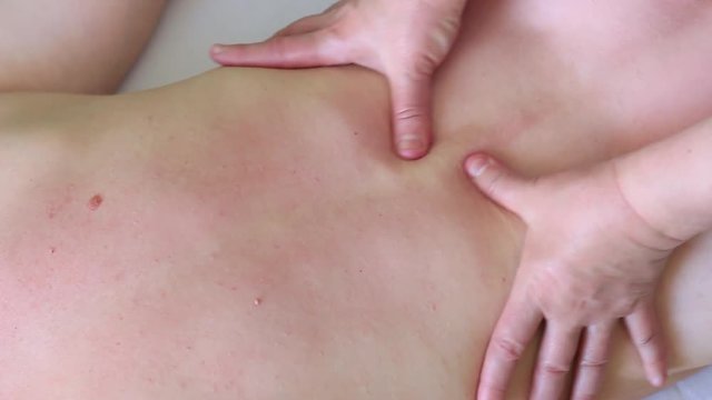 A woman-masseur makes a girl a therapeutic back massage along the spine.