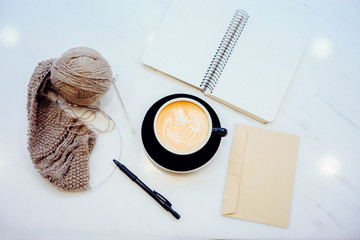 Top view of cappuccino, envelope,  ball of yarn pen and notebook  on white marble tabletop. Top view with copy space