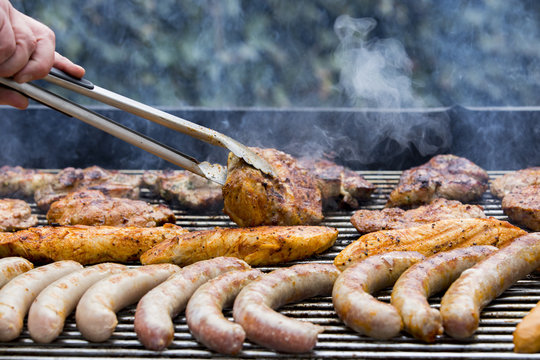 Fleisch und Wurst werden auf einem Grill zubereitet und mit einer Zange gewendet