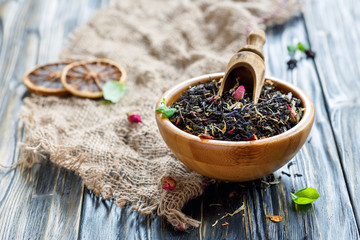 Scoop in wooden bowl with black tea and flower petals.