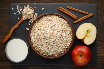 Rolled oat flakes in bowl with apple, cinnamon and milk on slate background. - 142636904