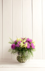 Flower bouquet in glass round vase on background of white wooden planks in provence style