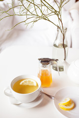 Cup of hot green tea with lemon on white table, fresh lemon and honey - closeup shot. Sun light flair effect. Nice interior in wooden house. Relaxation concept