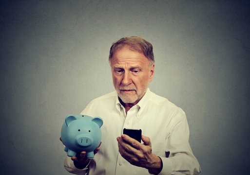 Preoccupied man looking at his mobile phone holding piggy bank