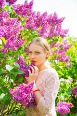 Beautiful blond young woman standing between blooming lilac bushes in spring garden