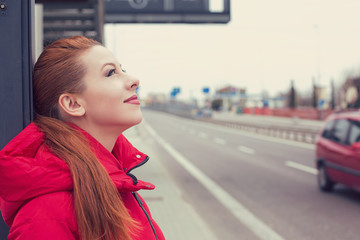 Portrait of happy woman standing outside at a bus stop, cute smiling