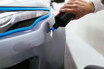 Car detailing - car polishing in auto repair shop. Front lights protected with isolation blue tape. Selective focus.