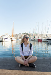 Pretty woman sitting alone at the seashore. Marina in the background