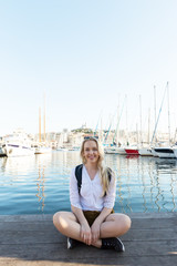 Pretty woman sitting alone at the seashore. Marina in the background