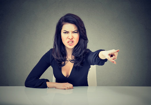 Angry business woman sitting at her desk and screaming pointing with finger to get out