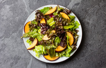 Vegetarian vegan lettuce salad with plums on black slate background. Top view