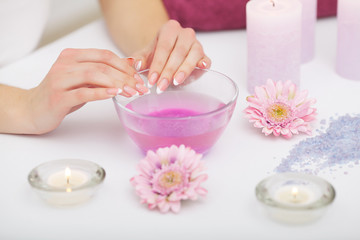 Obraz na płótnie Canvas Spa Procedure. Woman In Beauty Salon Holding Fingers In Aroma Bath For Hands. Closeup Of Female Nails Soaking In Bowl Of Water With Floating Pink Flower Petals. Skin Care. High Resolution