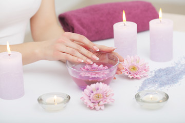 Obraz na płótnie Canvas Spa Procedure. Woman In Beauty Salon Holding Fingers In Aroma Bath For Hands. Closeup Of Female Nails Soaking In Bowl Of Water With Floating Pink Flower Petals. Skin Care. High Resolution