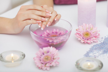 Spa Procedure. Woman In Beauty Salon Holding Fingers In Aroma Bath For Hands. Closeup Of Female Nails Soaking In Bowl Of Water With Floating Pink Flower Petals. Skin Care. High Resolution