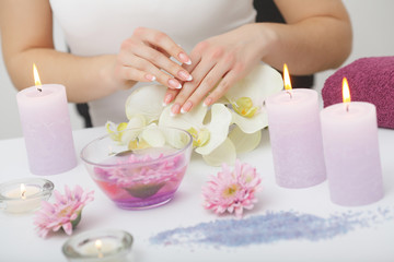 Fototapeta na wymiar Spa Beauty Salon. Closeup Of Female Hands With Perfect Natural Fingernails Soaking In Hand Bath Before Manicure. Woman Washing Perfect Nails In Transparent Bowl Of Water. Nail Care. High Resolution