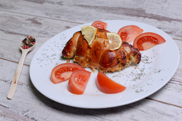 Baked chicken rolls with tomato and lemon and spices on white plate on a white wooden table