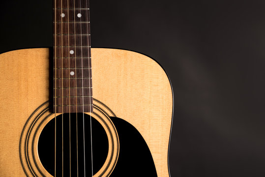 Part of a wooden acoustic guitar on the left side of the frame, on a black isolated background