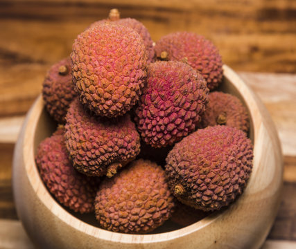 Unpeeled ripe red litchi fruits in wooden bowl