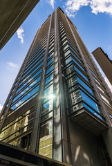 Fototapeta premium Shiny skyscraper against blue sky with white clouds on a sunny day