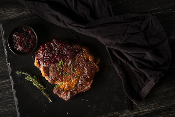 Beef steak and sauce with onion and herbs on black stone plate. Black table background with copy...