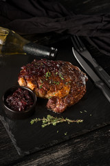 Steak and wine bottle with herbs on black stone plate. Black table background with copy text area for menu design. Vertical top view.