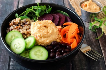 Healthy salad bowl with hummus, beans, wild rice, beets, carrots, cucumbers and pea shoots.