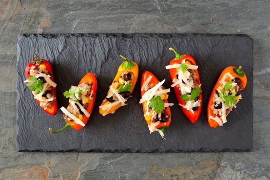 Fototapeta Stuffed mini peppers with wild rice, cheese, beans, corn and cilantro. Above view on a dark slate background.