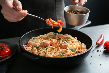 Woman adding sauce to chicken spaghetti in frying pan on table