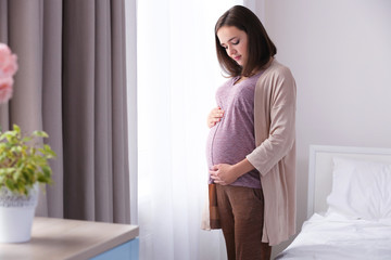 Naklejka premium Beautiful pregnant woman standing near window at home