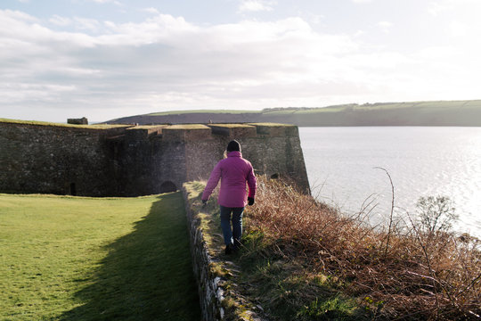 middle aged woman walks on stone wall on coast of Ireland