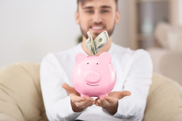 Happy young man sitting in armchair with piggy bank and money