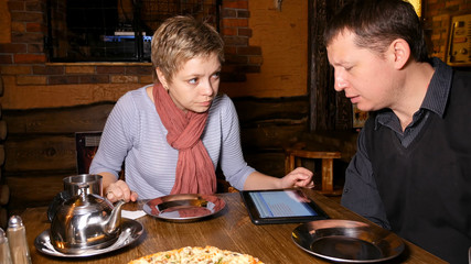 Businessman and businesswoman business partners discussing startup using tablet pad and chatting in a restaurant cafe.