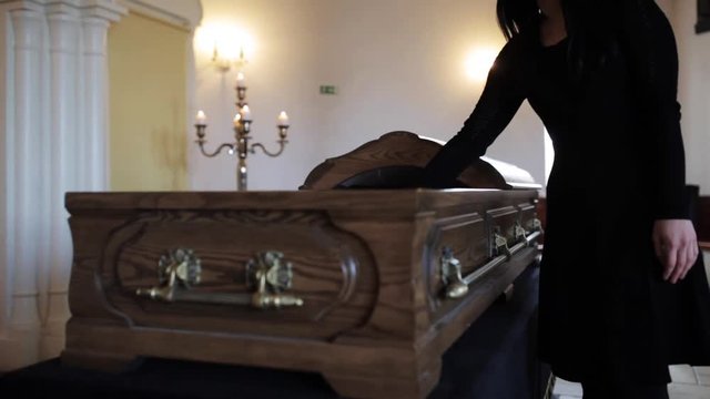 sad woman putting red rose into coffin at funeral