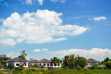 White cottages between palm trees under blue sky with clouds
