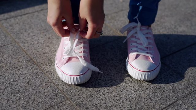  female hands tying shoelace on trendy pink gumshoes or  sneakers outdoors