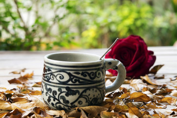 Coffee cup on dry leaves with rose