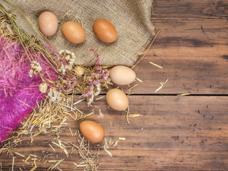 Rural eco background with brown chicken eggs, a piece of burlap, dry flowers and straw on the background of old wooden planks. The view from the top. Creative background for Easter cards or menu